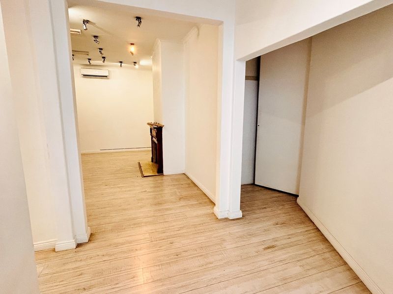 An open-plan office space featuring light-toned laminate flooring, track lighting, and a split-system air conditioner, offering a clean and versatile workspace.