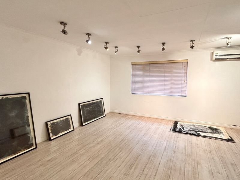 A bright, empty office space featuring laminate flooring, track lighting, and a wall-mounted split-system air conditioner.