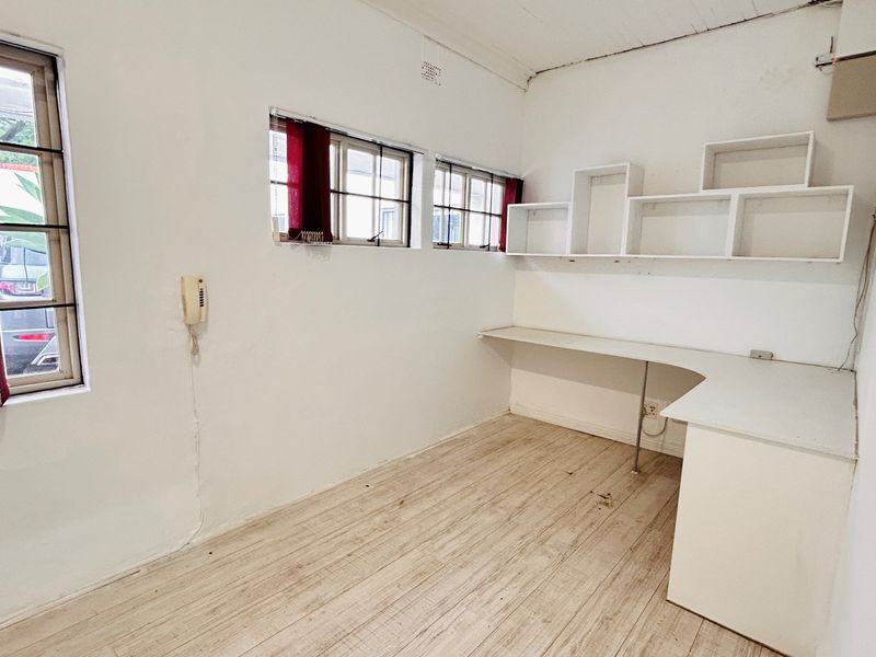 A functional office space featuring built-in desk and shelving units, laminate flooring, and multiple windows providing natural light.