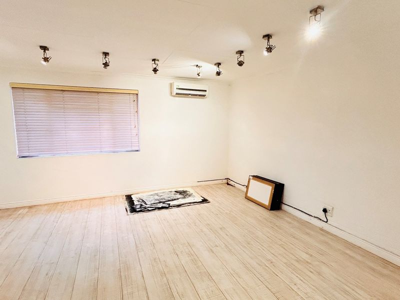A bright, empty office space featuring laminate flooring, track lighting, and a wall-mounted air conditioning unit.