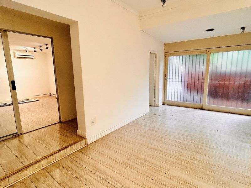 An empty office space featuring laminate flooring, sliding glass doors, and an integrated air conditioning unit, offering a clean and versatile workspace.