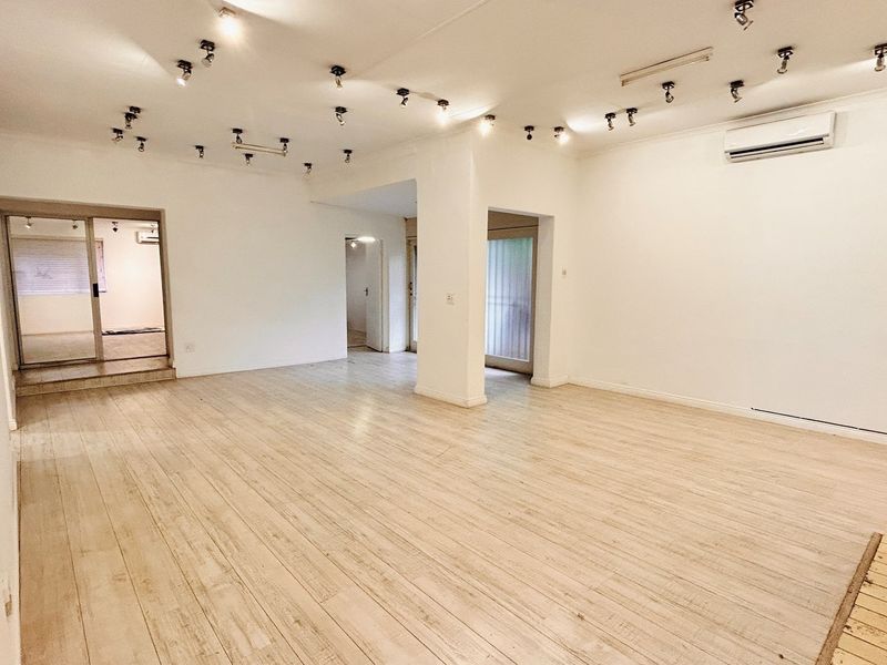 Spacious, open-plan office area featuring light-toned laminate flooring, multiple track lighting fixtures, and a wall-mounted air conditioning unit.