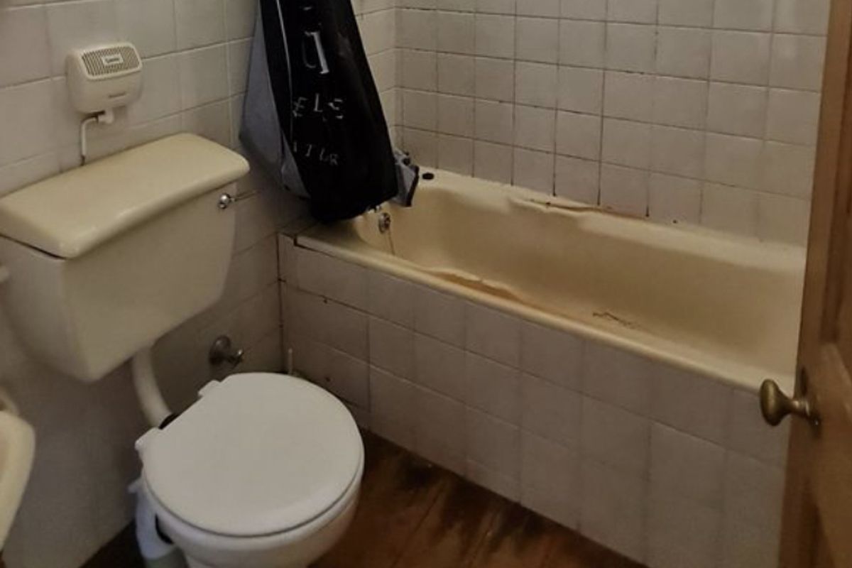 A dated bathroom featuring a standard toilet and a built-in bathtub with wall tiling, requiring significant refurbishment and modernization of fixtures and finishes.