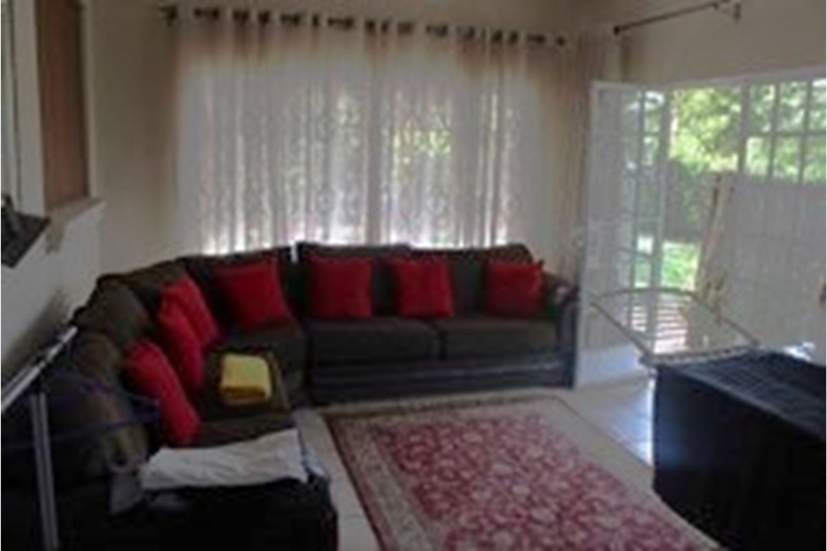 A living room area featuring tiled flooring, large windows with curtains, and access to an outdoor space through a glass-paned door.