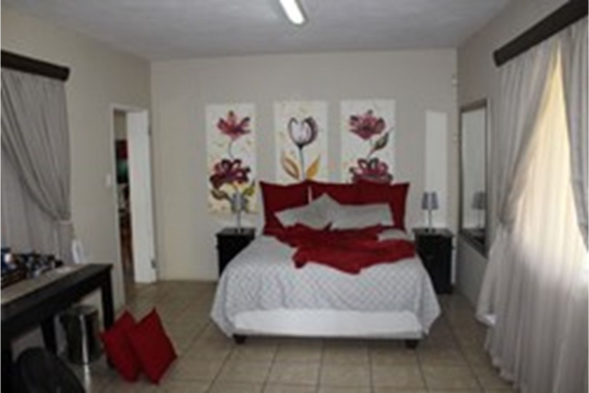 A spacious bedroom featuring tiled flooring, neutral wall tones, and large windows with curtain treatments.
