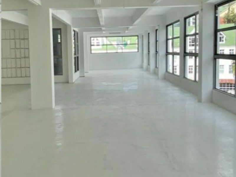A spacious, open-plan commercial office area featuring polished concrete floors, exposed ceiling beams, and large windows providing ample natural light.