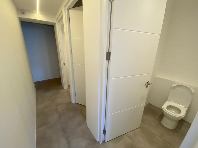 A clean, modern hallway featuring tiled flooring, recessed lighting, and access to a private restroom with a modern toilet suite.