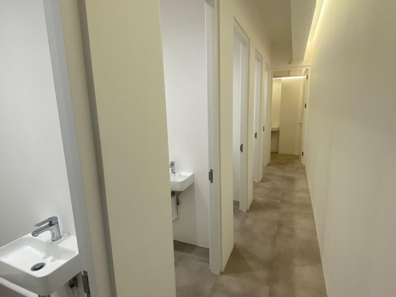 A clean, modern commercial hallway featuring multiple individual restroom cubicles, each equipped with a wall-mounted basin and integrated lighting.