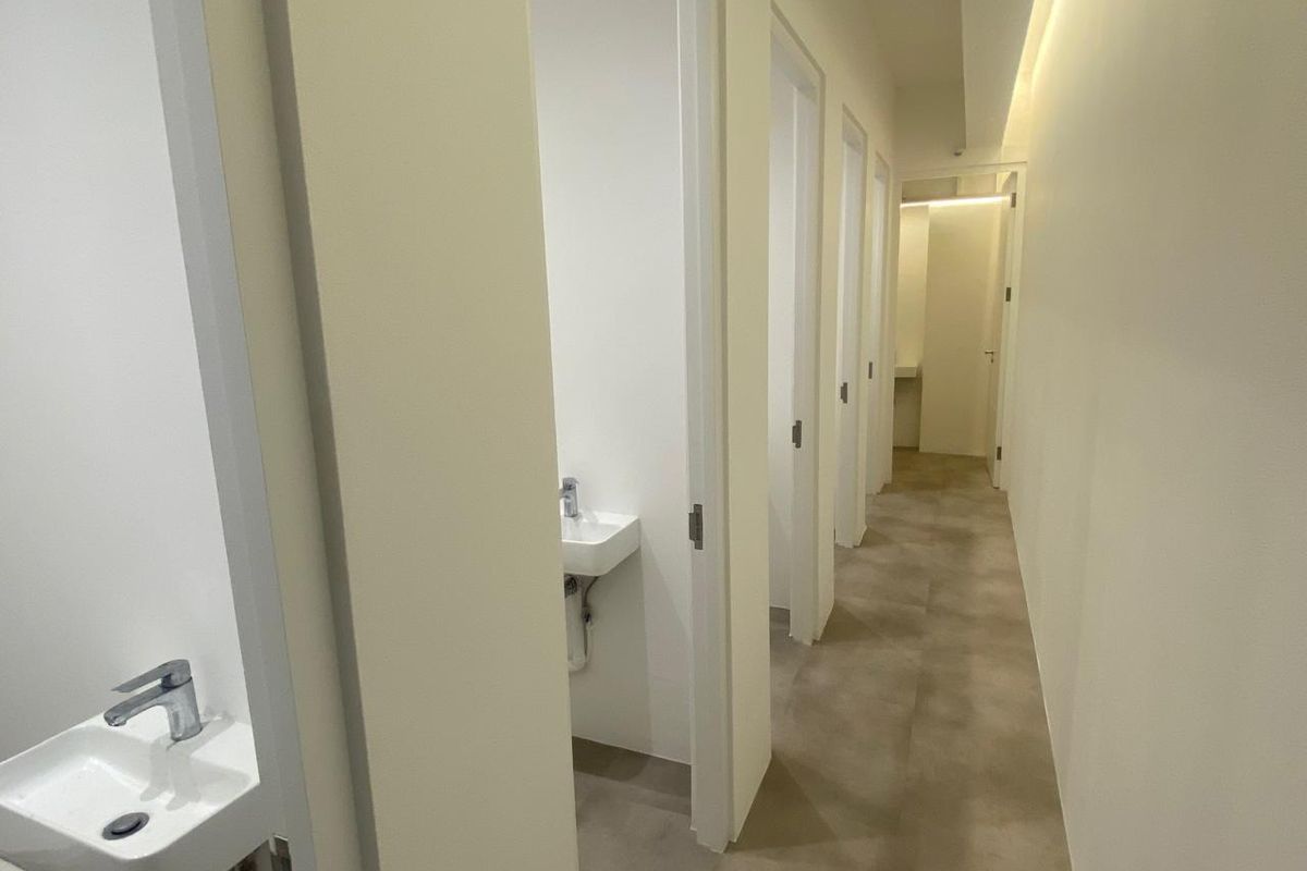 A clean, modern commercial hallway featuring multiple individual restroom cubicles, each equipped with a wall-mounted basin and integrated lighting.
