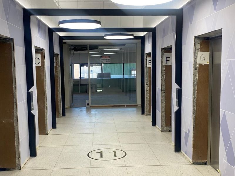 A commercial office elevator lobby featuring tiled flooring, modern circular lighting, and multiple elevator access points currently undergoing renovation.