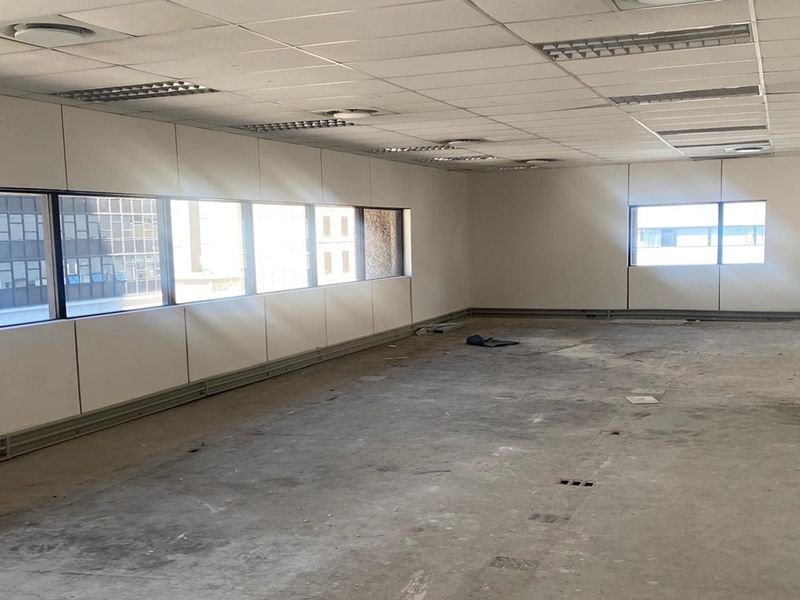 An empty, open-plan office space featuring a suspended ceiling, recessed lighting, and large windows with perimeter trunking, requiring floor refurbishment.