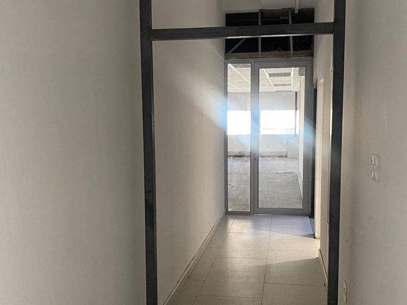 A vacant office hallway featuring a metal-framed glass door and tiled flooring, currently showing an unfinished ceiling area.