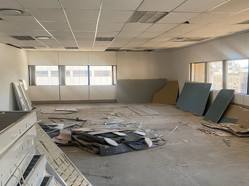 An empty office space currently undergoing renovation, featuring a suspended ceiling and large windows, requiring significant finishing work to be functional.