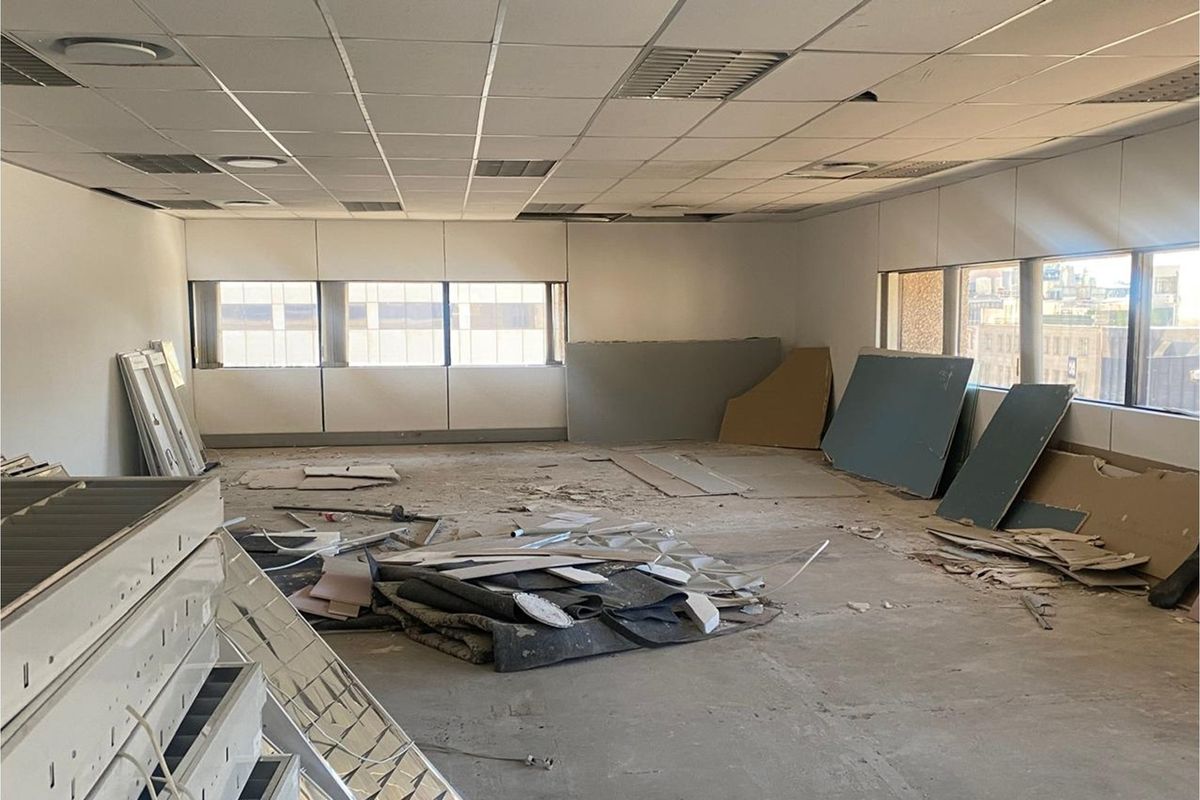 An empty office space currently undergoing renovation, featuring a suspended ceiling and large windows, requiring significant finishing work to be functional.