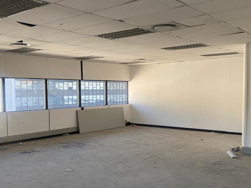 An empty, open-plan office space featuring large windows, suspended ceilings with recessed lighting, and unfinished flooring, ready for renovation or custom fit-out.