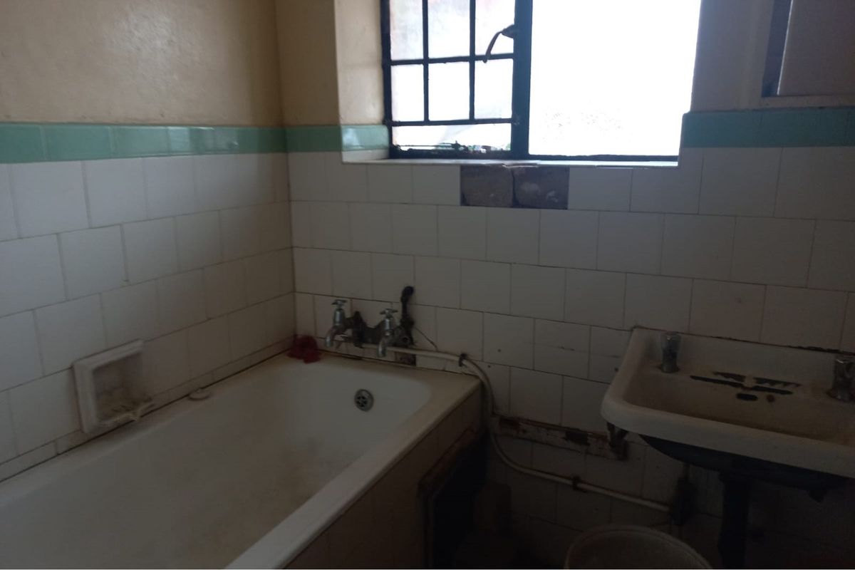A dated bathroom featuring a bathtub and wall-mounted basin, requiring significant renovation and repair to the tiling and plumbing fixtures.