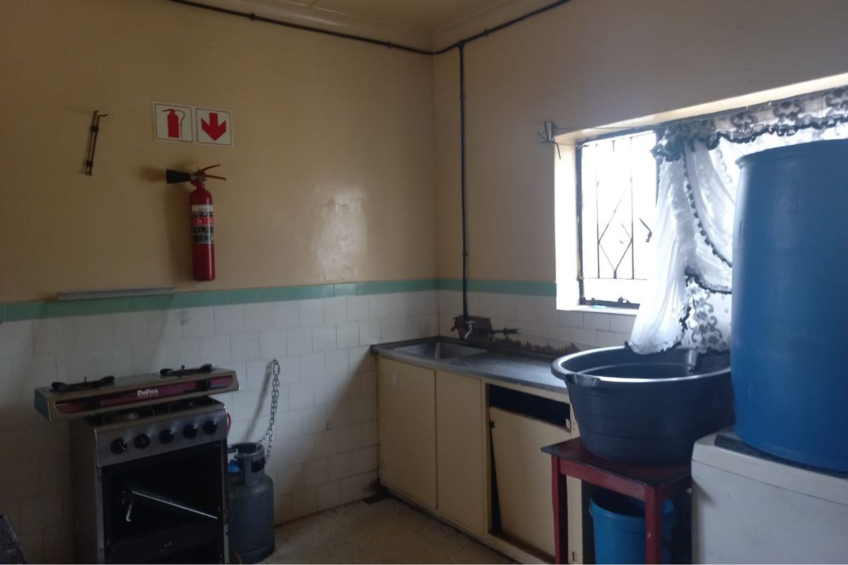 A functional kitchen area featuring a built-in sink, tiled splashback, and space for a gas stove, requiring cosmetic updates and maintenance.