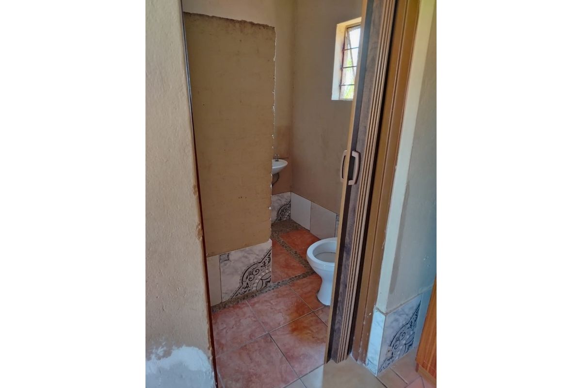 A compact bathroom featuring a standard toilet and wall-mounted basin with tiled flooring and neutral wall finishes.