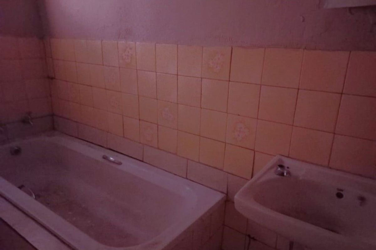 A dated bathroom featuring a built-in bathtub and pedestal sink with original wall tiling, requiring significant renovation and modernization.