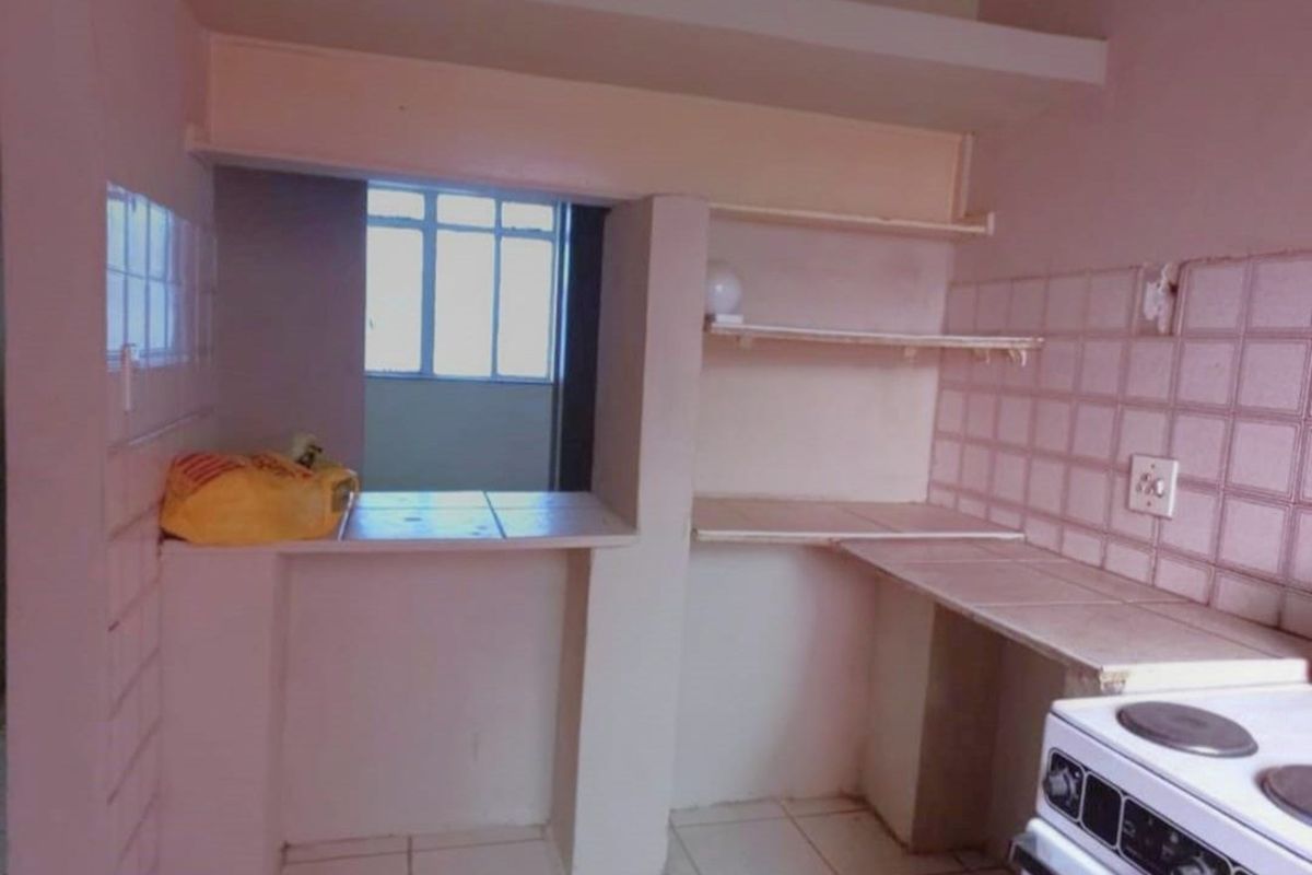 A compact kitchen area featuring built-in tiled countertops, open shelving, and a tiled backsplash, providing a functional prep space.