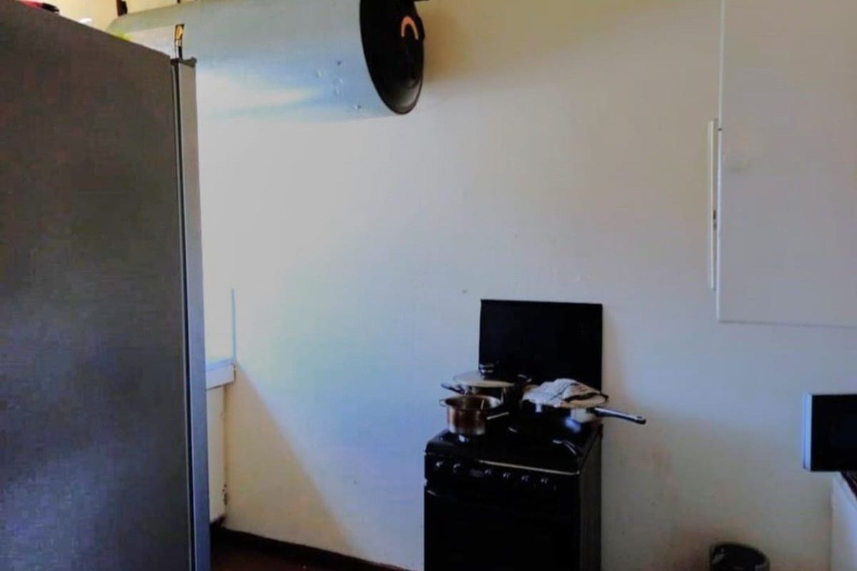 A compact kitchen area featuring a freestanding stove and wall-mounted extractor fan, requiring cosmetic updates to improve the overall finish.