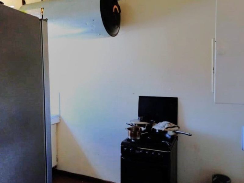 A compact kitchen area featuring a freestanding stove and wall-mounted extractor fan, requiring cosmetic updates to improve the overall finish.