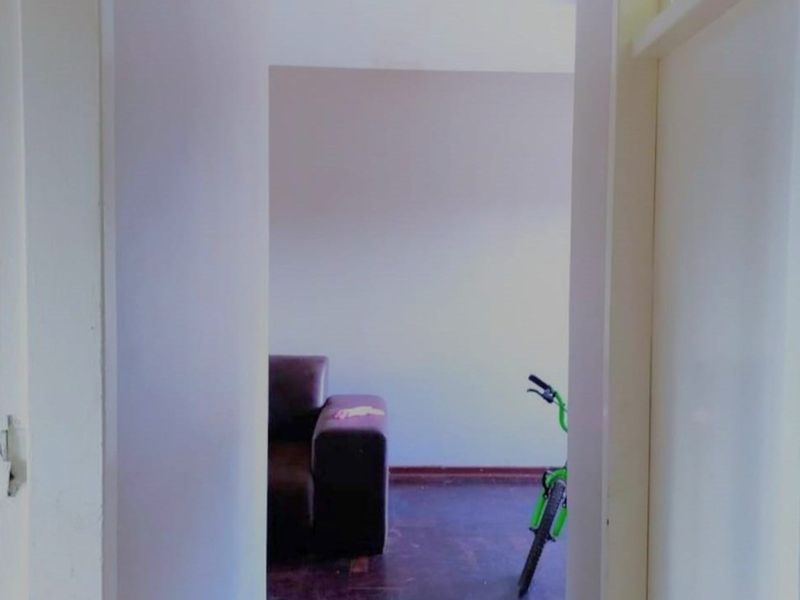 A view through a doorway into an empty room featuring dark parquet flooring and plain walls, showing signs of wear.