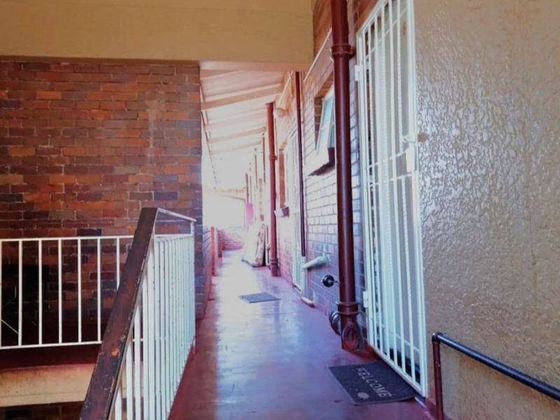 An exterior covered walkway featuring brick walls, metal security gates, and metal railings, providing access to the retail or residential units.