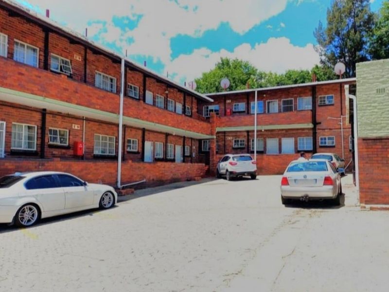 Rear exterior view of a multi-story brick retail or residential complex featuring a paved courtyard area and security bars on windows.