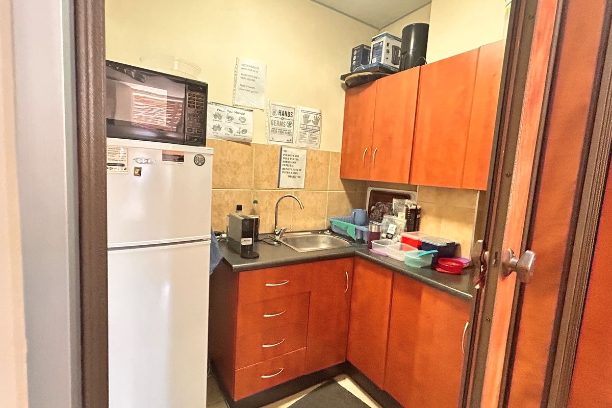 A compact kitchenette featuring wooden cabinetry, a stainless steel sink, and tiled splashback, suitable for a small office or retail utility space.