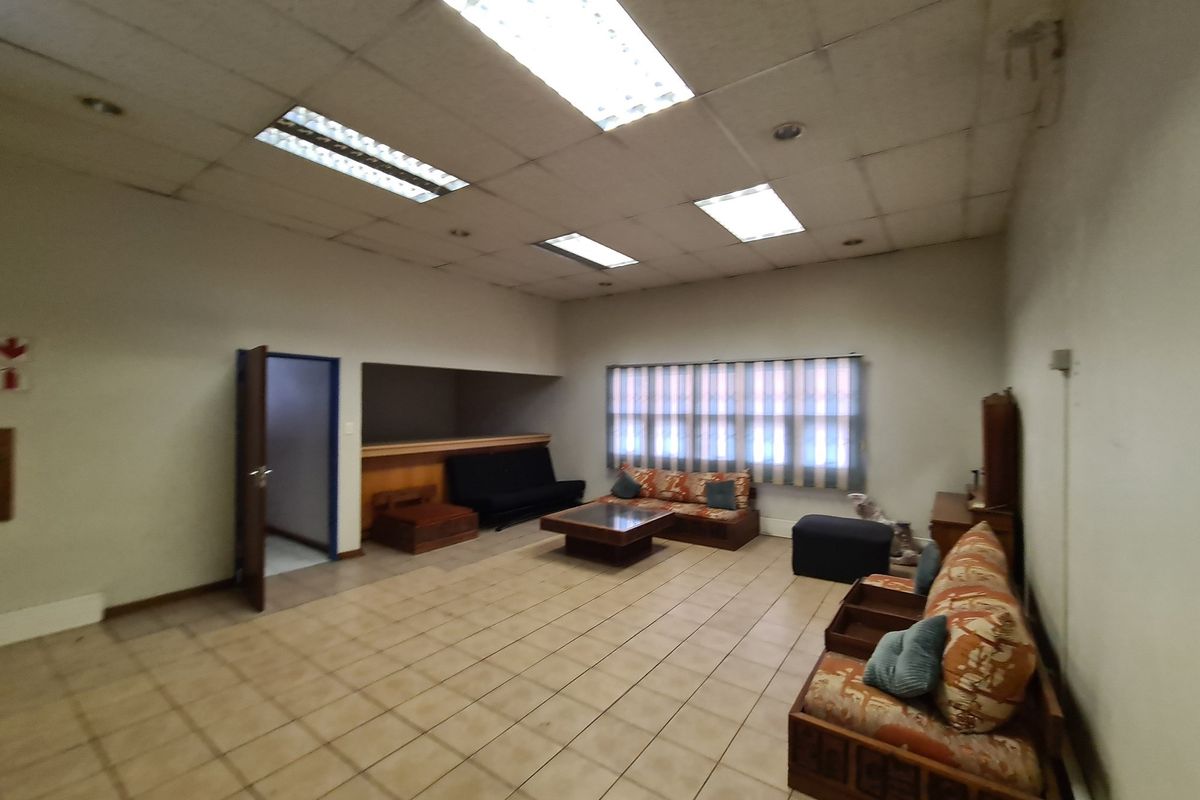 Spacious living area featuring tiled flooring, suspended ceiling with integrated lighting, and window blinds, offering a functional space ready for modernization.
