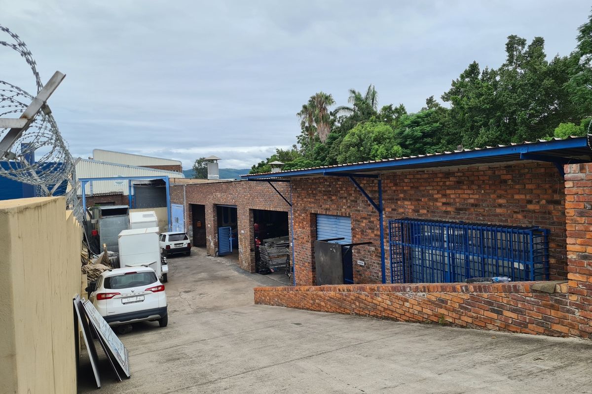 Rear industrial yard featuring exposed brick warehouse units, metal roller shutter doors, concrete driveway, and secure perimeter fencing with razor wire.