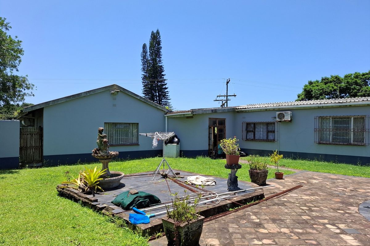 Rear view of the property featuring a paved patio area, lawn, and exterior building facade with security bars on windows.