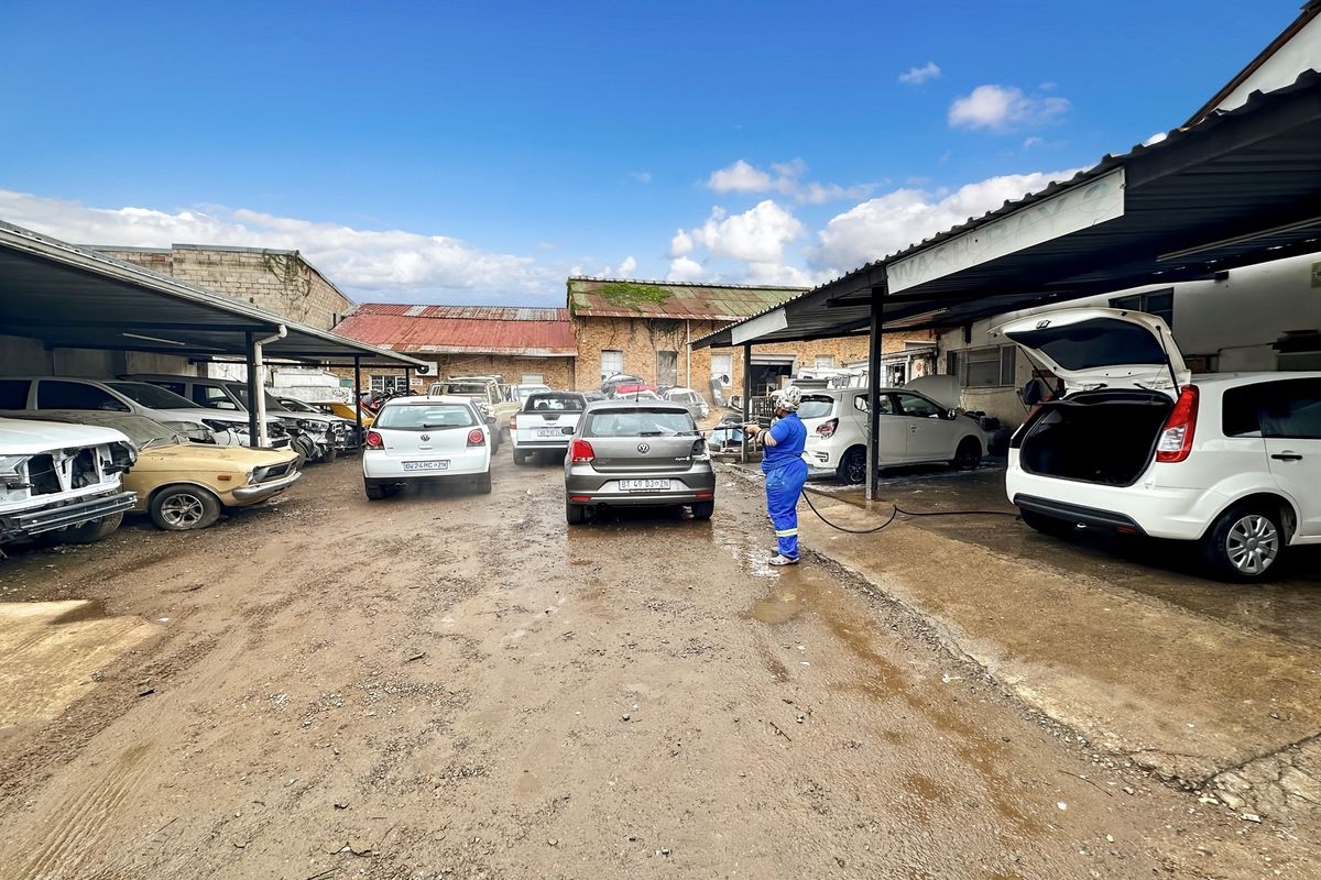 Outdoor commercial service area featuring covered bays, unpaved ground, and industrial building structures suitable for automotive operations.