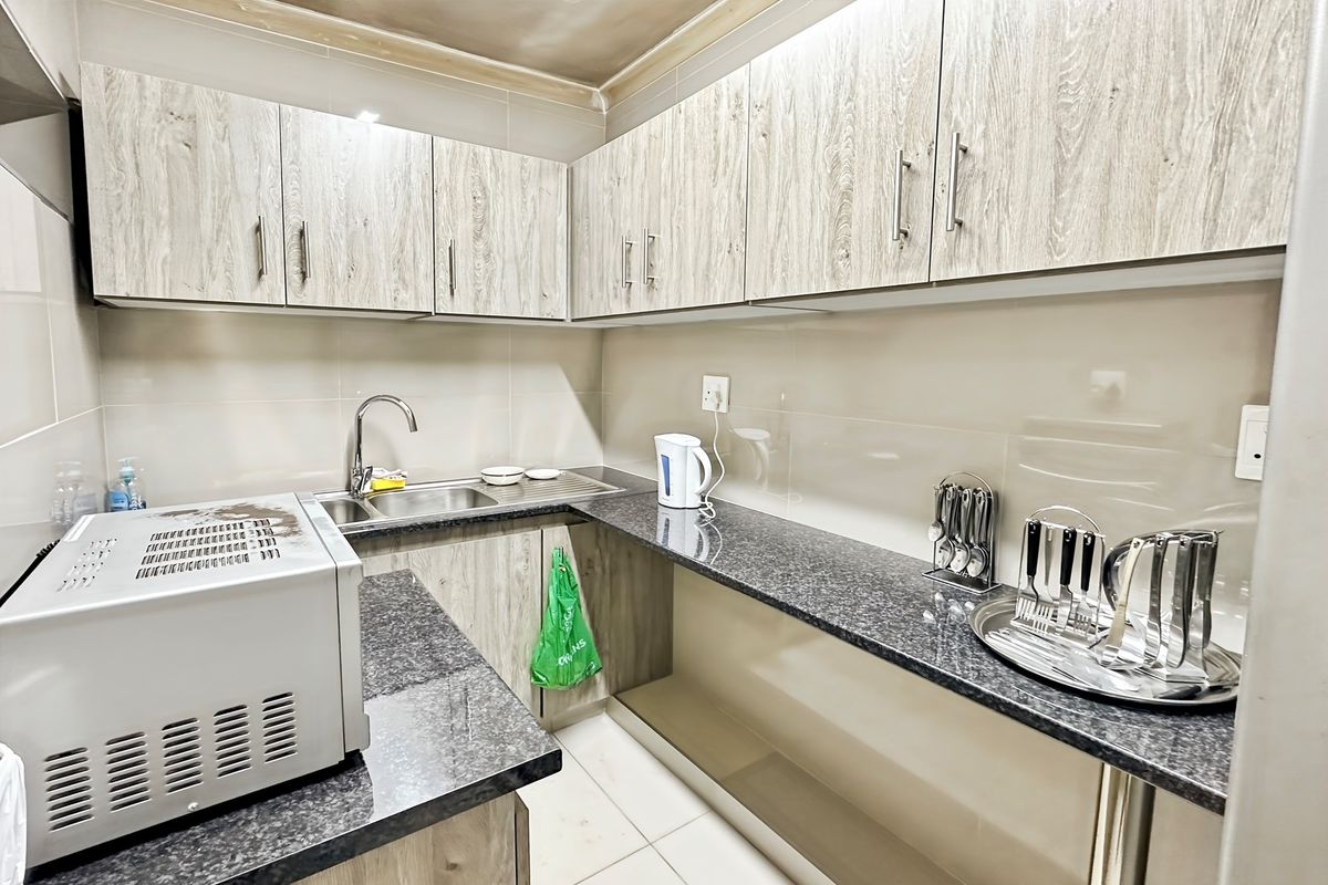 Compact kitchen featuring wood-grain cabinetry, granite countertops, stainless steel sink, and tiled backsplash.