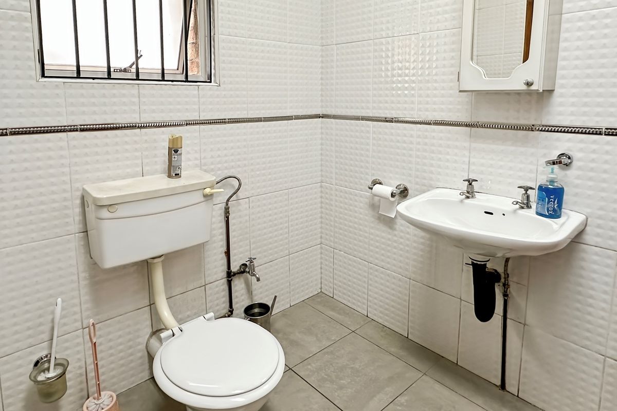 A functional bathroom featuring a wall-mounted basin, standard toilet, and full-height wall tiling with a decorative border.
