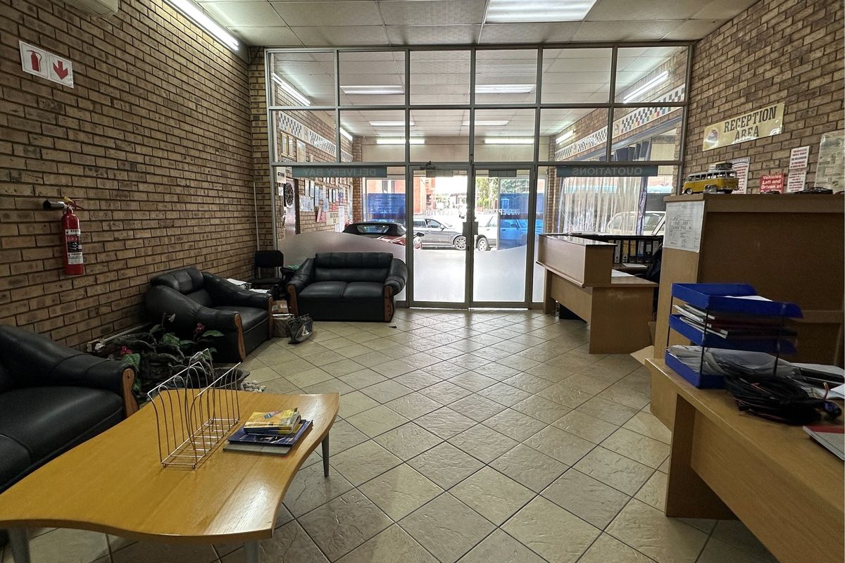 A functional retail reception area featuring exposed brick walls, tiled flooring, and large glass entrance doors providing natural light and street visibility.