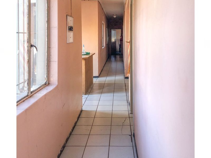 A long, empty commercial hallway featuring tiled flooring and painted walls, showing signs of wear and requiring maintenance.