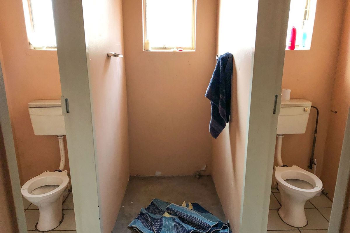 A commercial bathroom facility featuring two toilet stalls with cisterns and a central open stall, requiring cosmetic updates and maintenance.