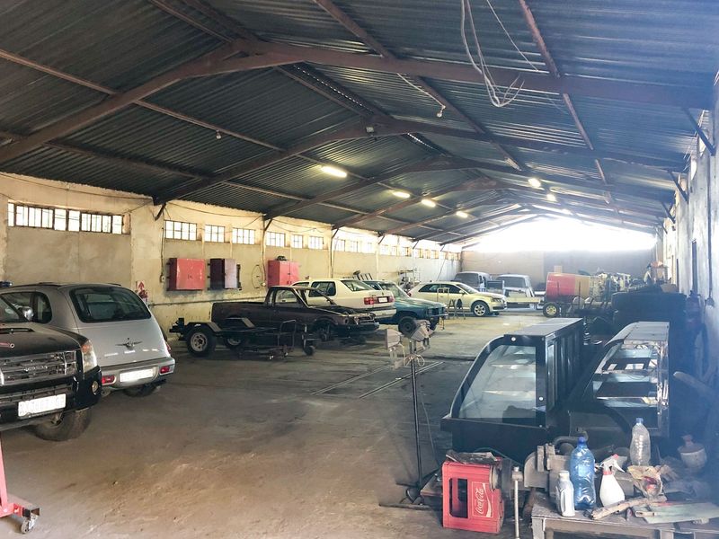 Spacious industrial garage or workshop featuring exposed steel roof trusses, concrete flooring, and high-level windows, suitable for automotive or storage use.