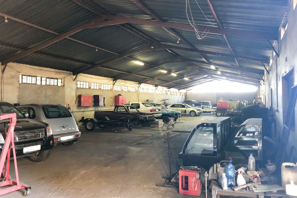 Spacious industrial garage or workshop featuring exposed steel roof trusses, concrete flooring, and high-level windows, suitable for automotive or storage use.