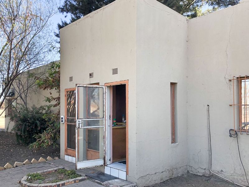 Rear exterior view of the commercial property featuring plastered walls, security gates, and window bars, showing signs of wear and maintenance requirements.