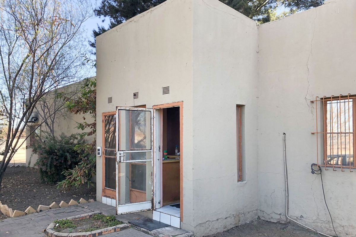 Rear exterior view of the commercial property featuring plastered walls, security gates, and window bars, showing signs of wear and maintenance requirements.
