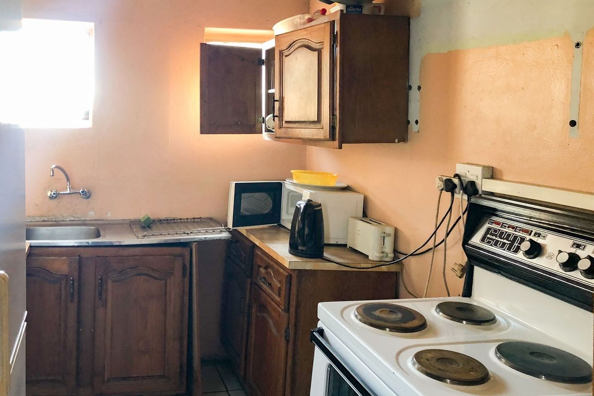 A dated kitchen featuring wooden cabinetry, a stainless steel sink, and an electric stove, requiring cosmetic updates and finish improvements.