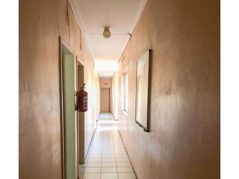 A narrow commercial hallway featuring tiled flooring, a wall-mounted fire extinguisher, and dated wall finishes requiring maintenance and cosmetic updates.