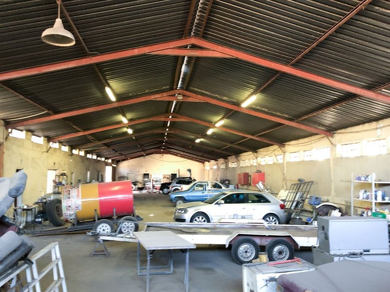 Spacious industrial warehouse or workshop featuring high-pitched corrugated metal roofing, exposed steel trusses, and concrete flooring, suitable for commercial or storage use.