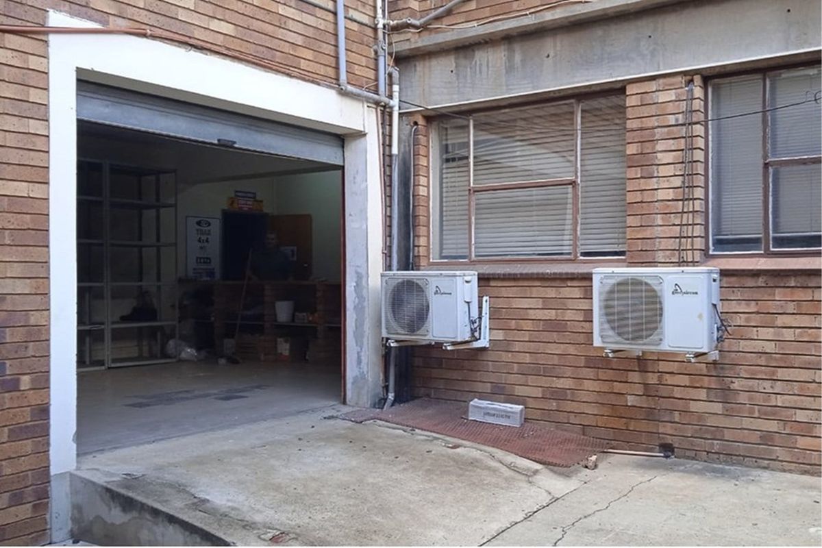 Exterior view of a retail property featuring a garage-style entrance, brick facade, and two wall-mounted air conditioning units.
