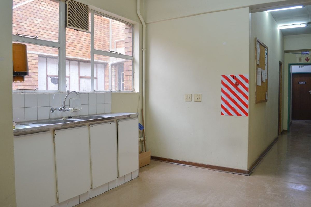 A functional kitchenette area featuring a stainless steel sink, built-in cabinetry, and a window overlooking an exterior brick wall.