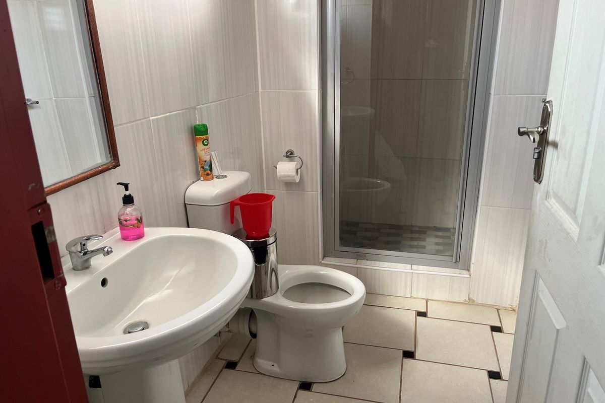 A functional bathroom featuring a pedestal basin, a standard toilet, and a glass-enclosed shower with tiled walls and flooring.