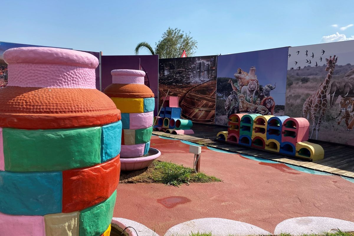 Outdoor recreational area featuring decorative painted structures, wooden decking, and large printed wall panels in a retail or commercial setting.